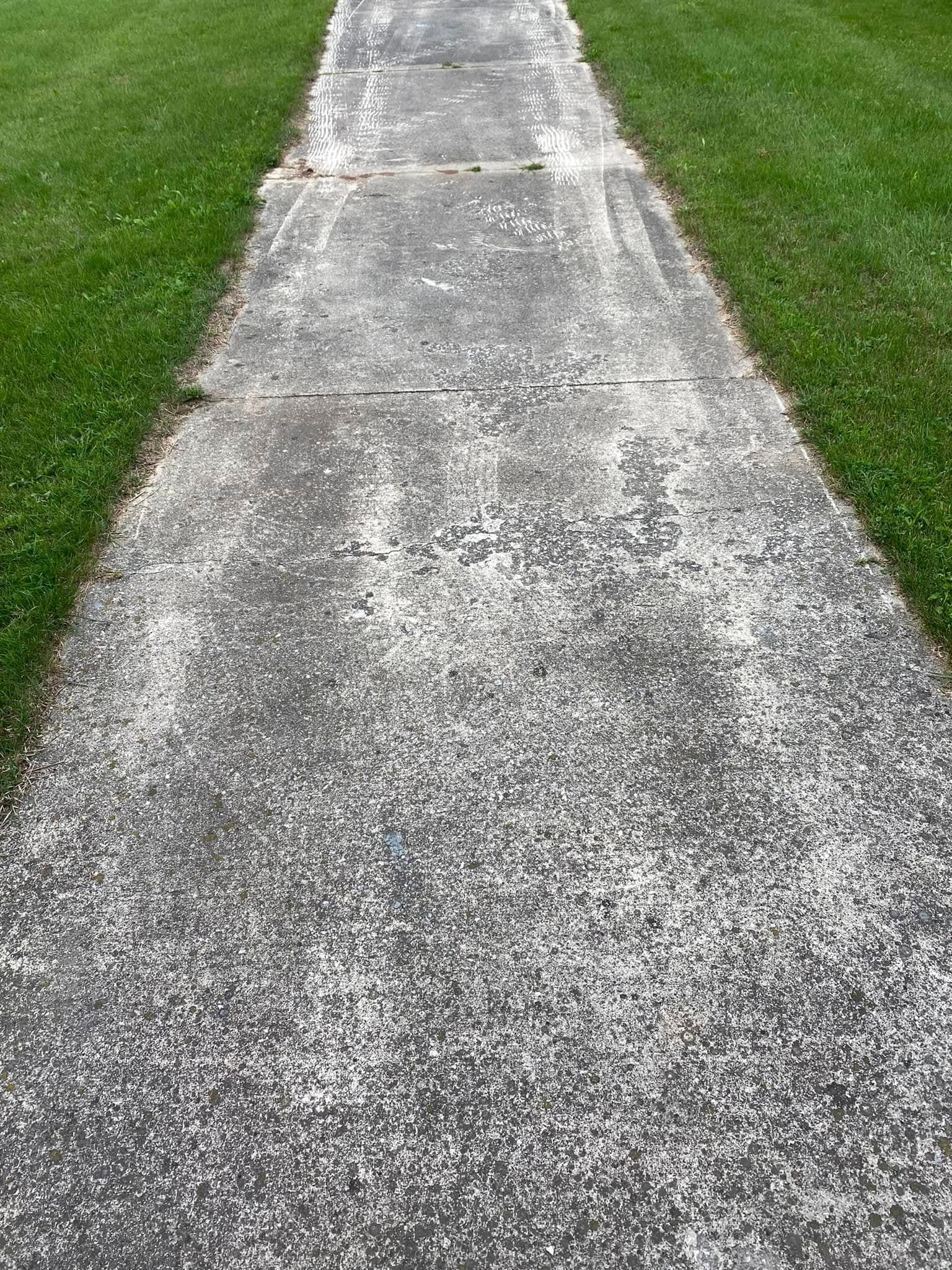 Uneven concrete sidewalk surrounded by green grass, showing signs of wear and usage.