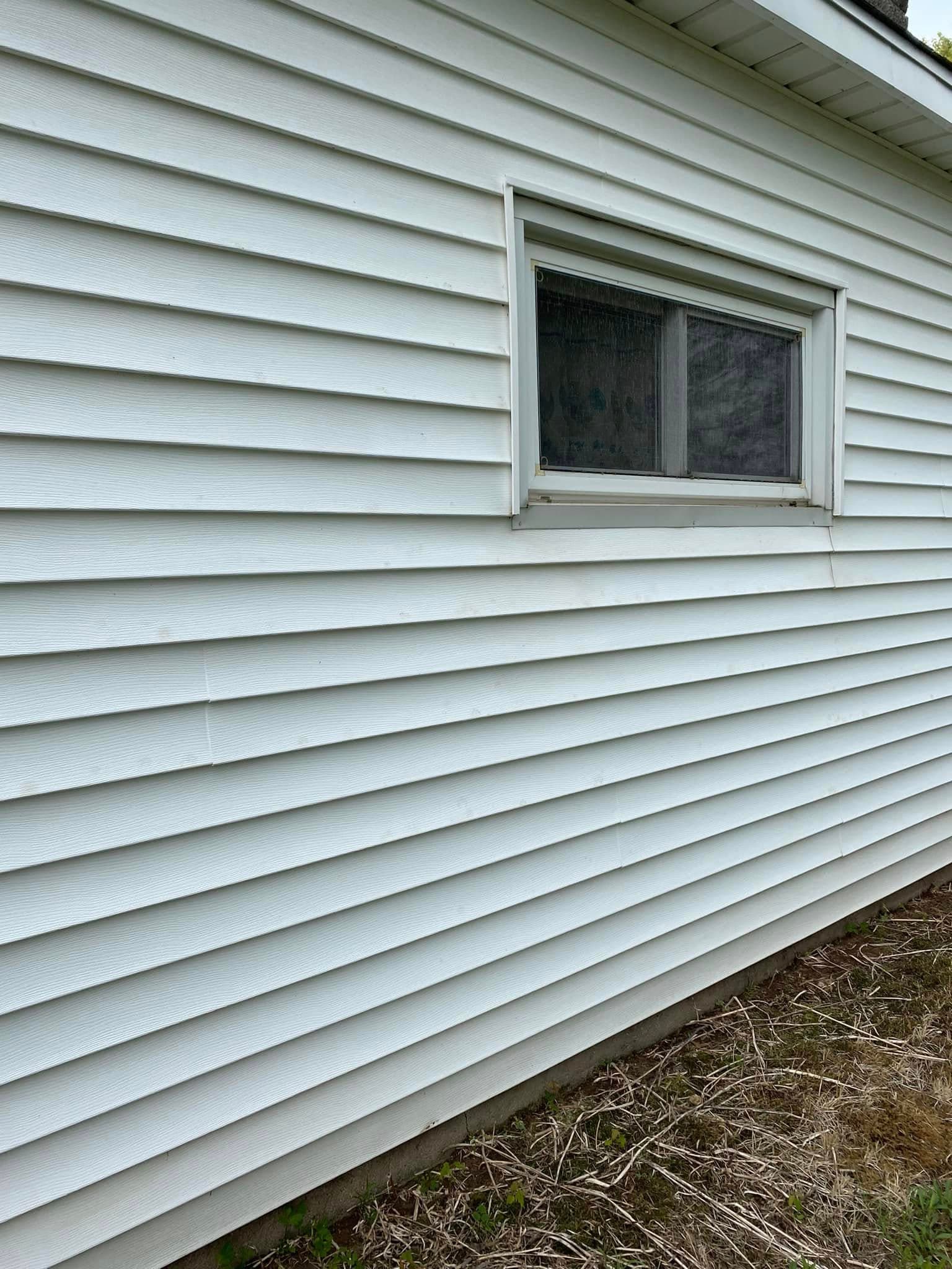 Side view of a house showing white vinyl siding and a small window.
