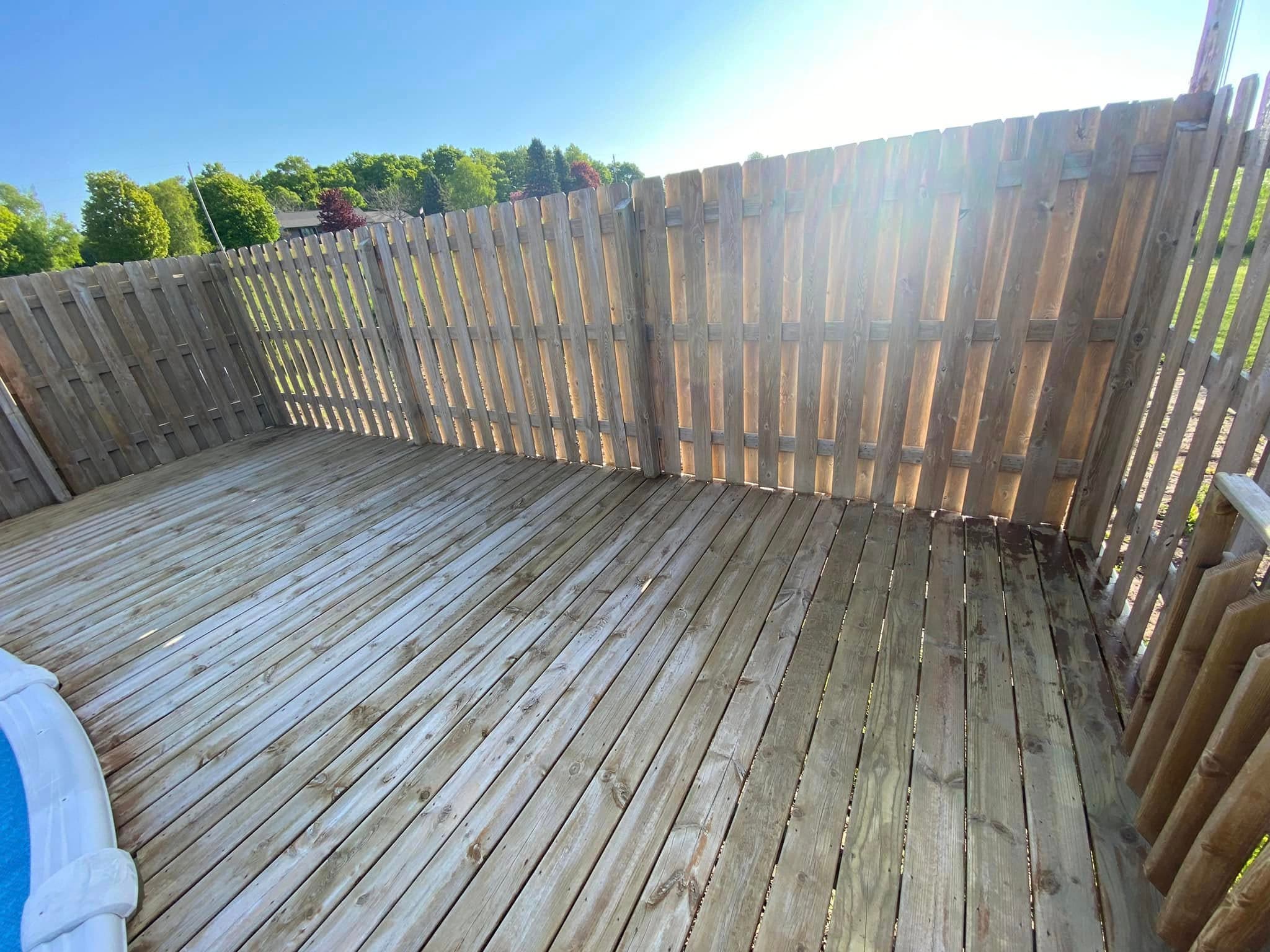 Wooden deck with a pool in bright sunlight and a wooden fence in the background.