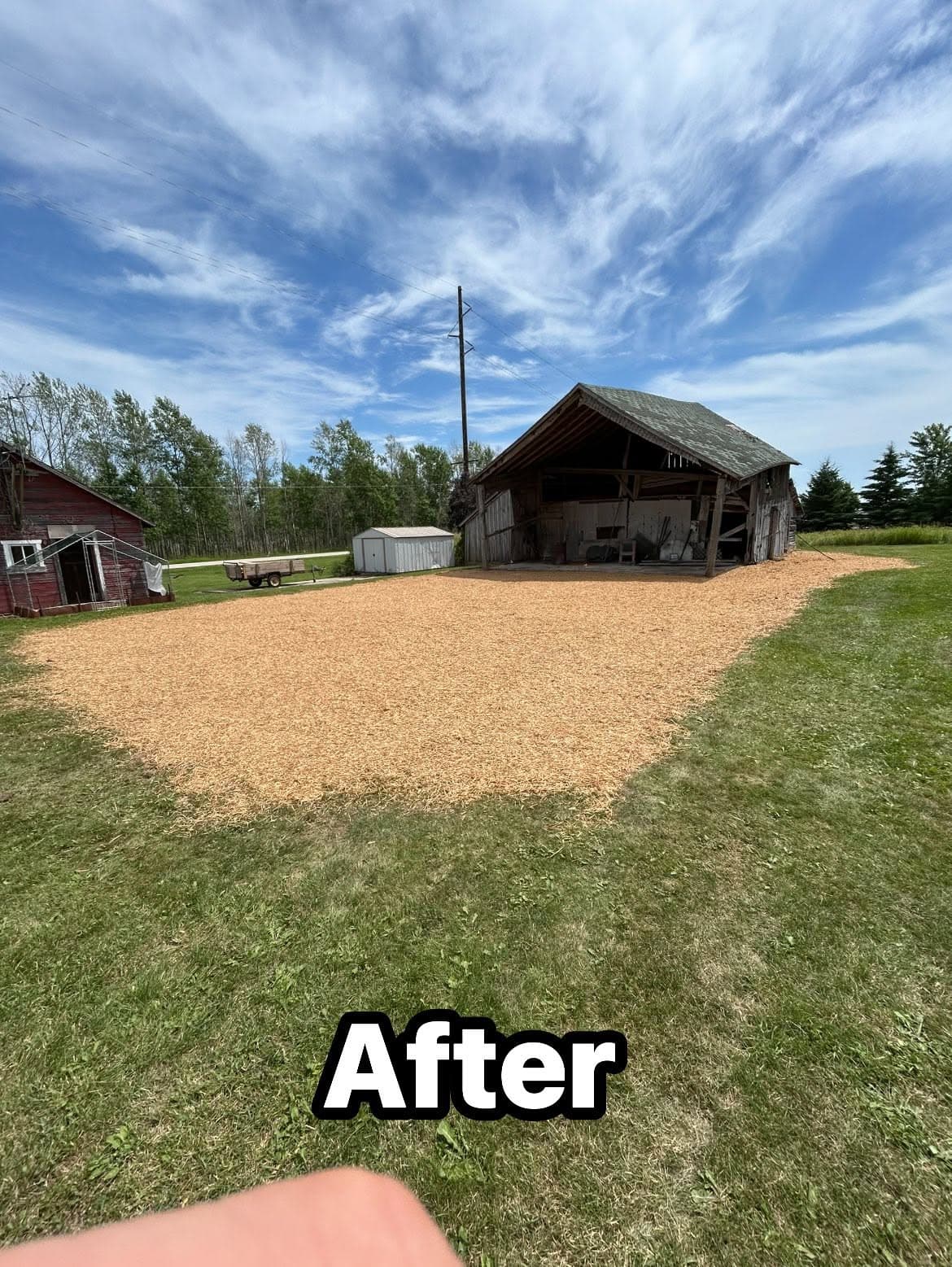 Landscaped area with wood chips, showcasing improvements around a barn under a clear sky.