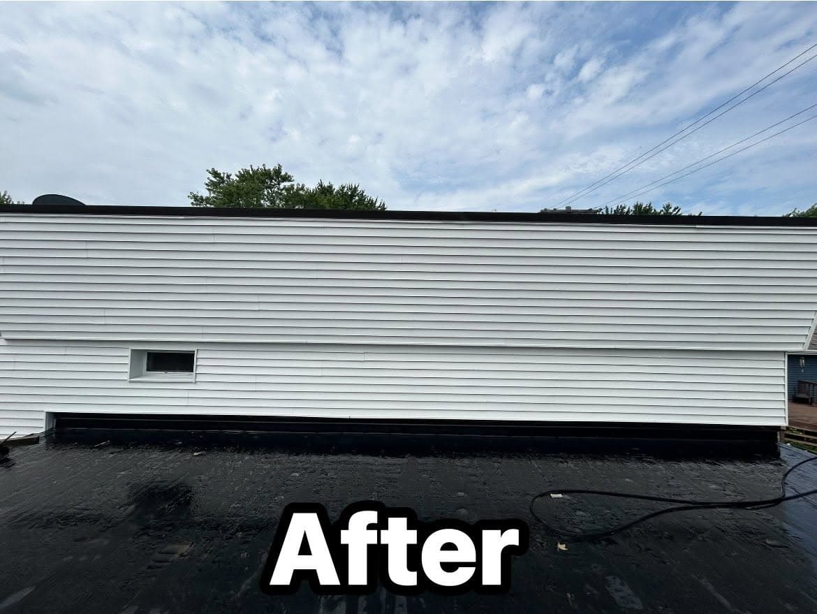 Renovated flat roof with new drainage system and clean, white siding under a cloudy sky.