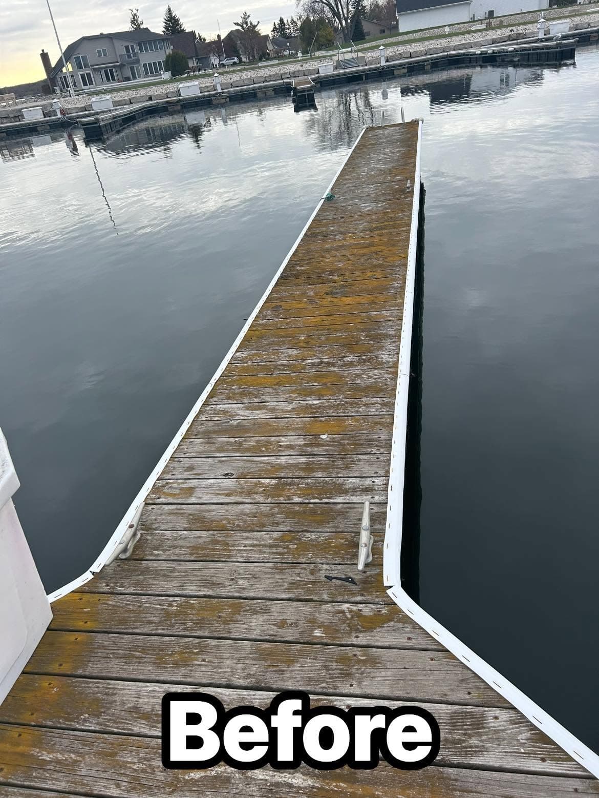 Wooden dock before restoration at calm marina with clear water and cloudy sky.