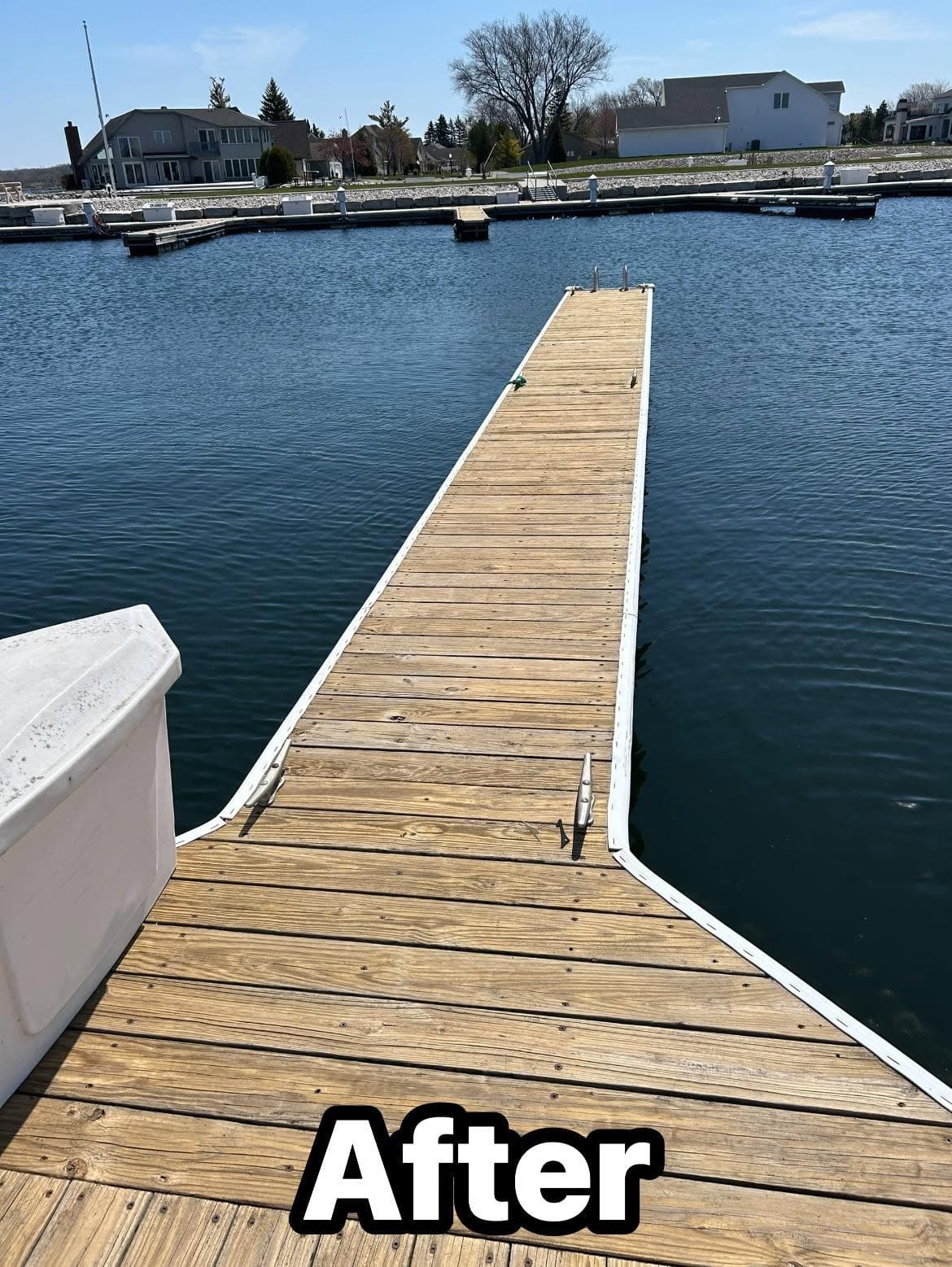 Wooden dock extending over calm water at a marina, with a clear blue sky above.