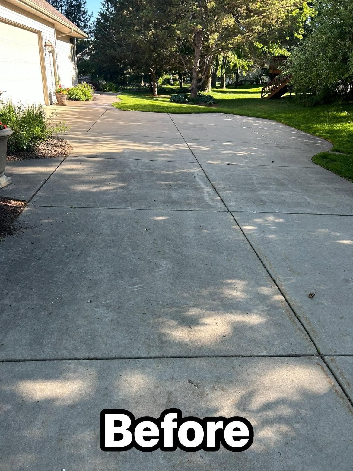 Driveway before cleaning, showing uneven surface and faded concrete. Lush green landscaping nearby.
