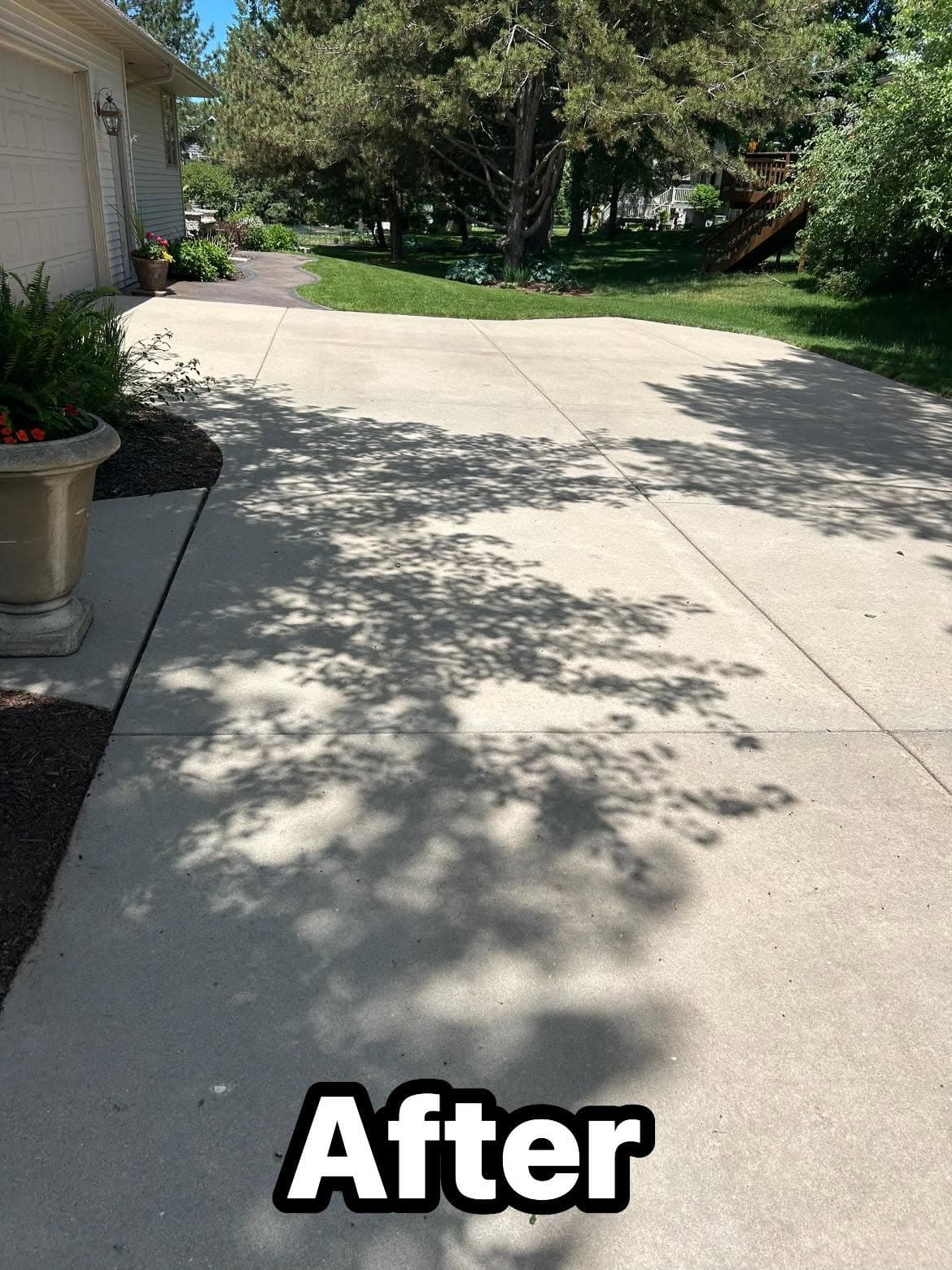 Clean, finished concrete driveway with visible shadows and landscaped surroundings.
