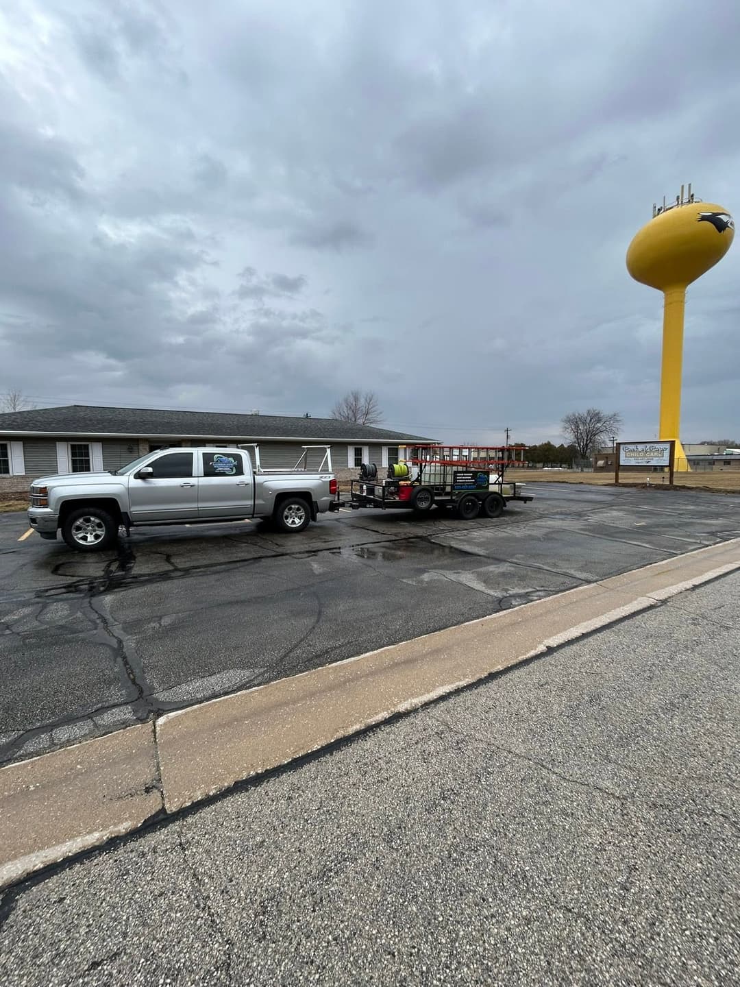 Pickup truck with trailer parked near a yellow water tower on a cloudy day.