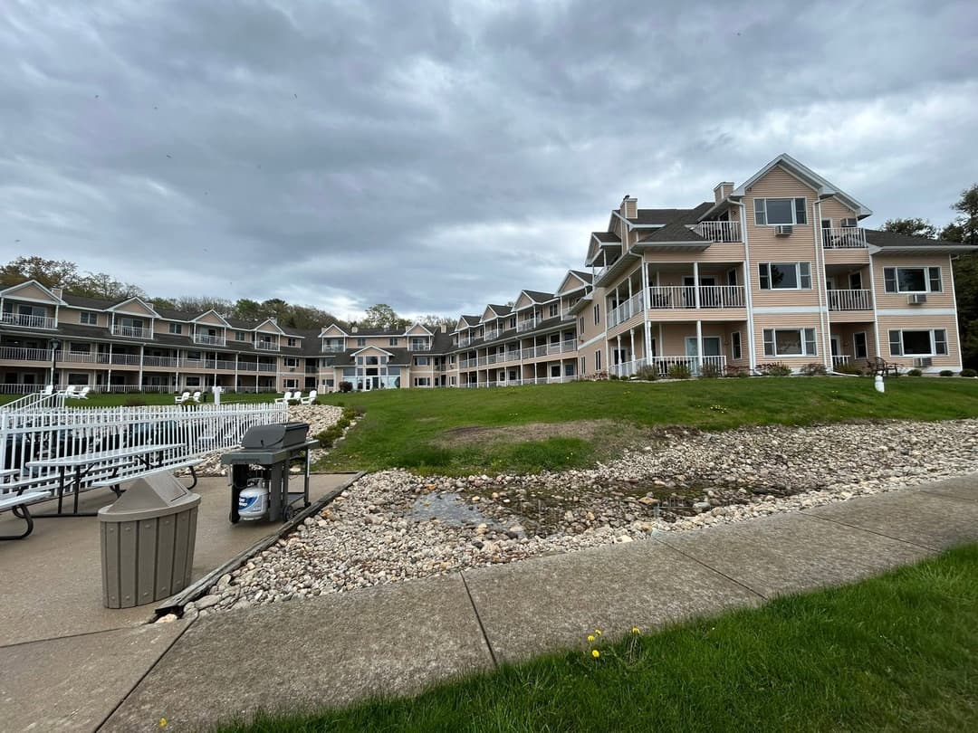 Modern lakeside condos with grassy area, stone path, and cloudy sky. Ideal for relaxation.