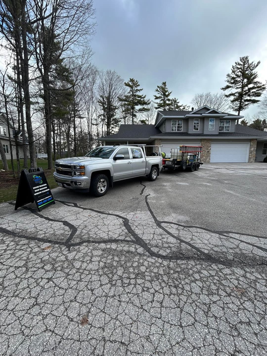 Silver pickup truck with trailer parked in front of a house surrounded by trees.