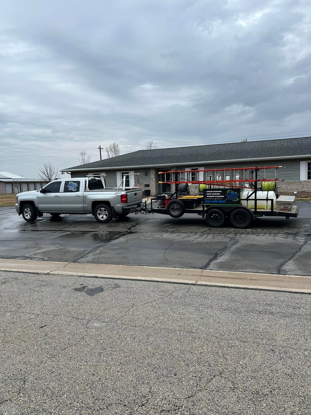 Silver pickup truck towing a trailer with equipment parked in a lot on a cloudy day.