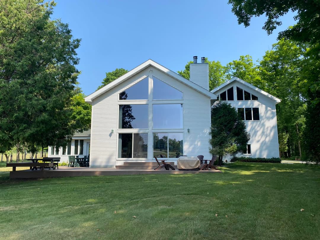 Modern white house with large windows, surrounded by greenery and a manicured lawn.