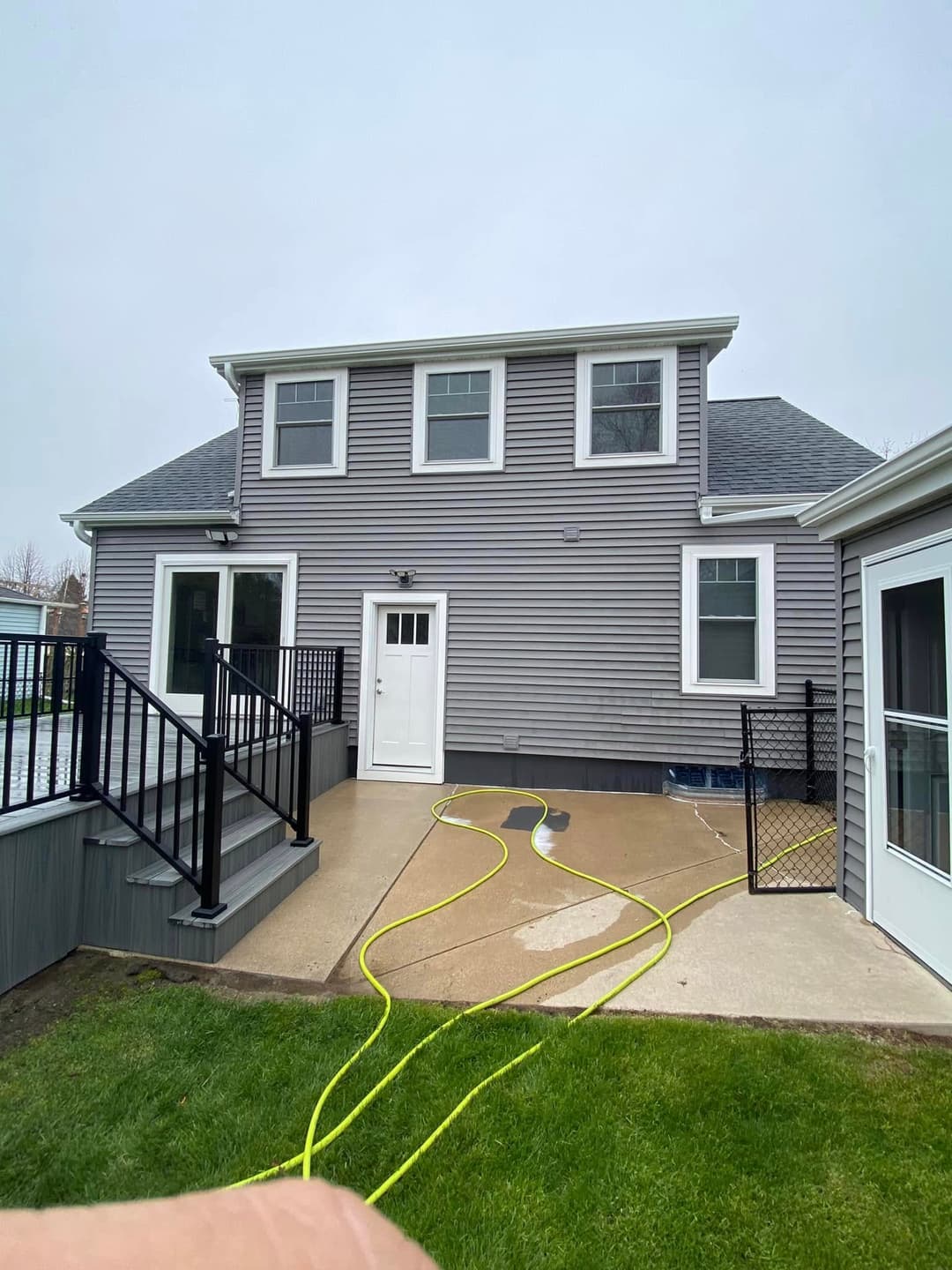 Two-story gray house exterior with a patio and hose on the ground in a residential setting.