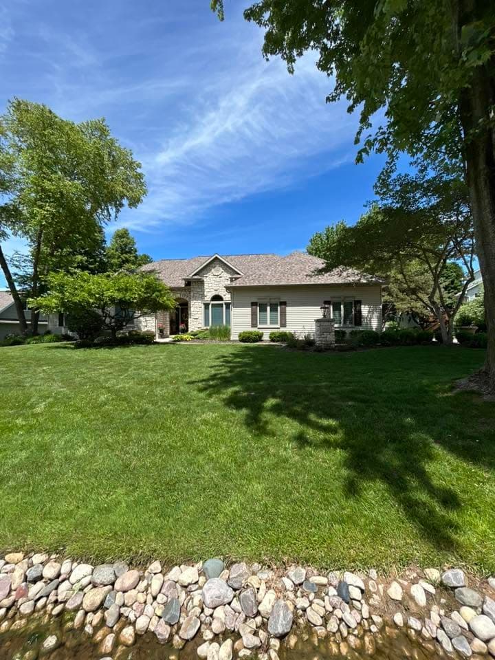 Charming home with landscaped yard and rocky creek under a clear blue sky.