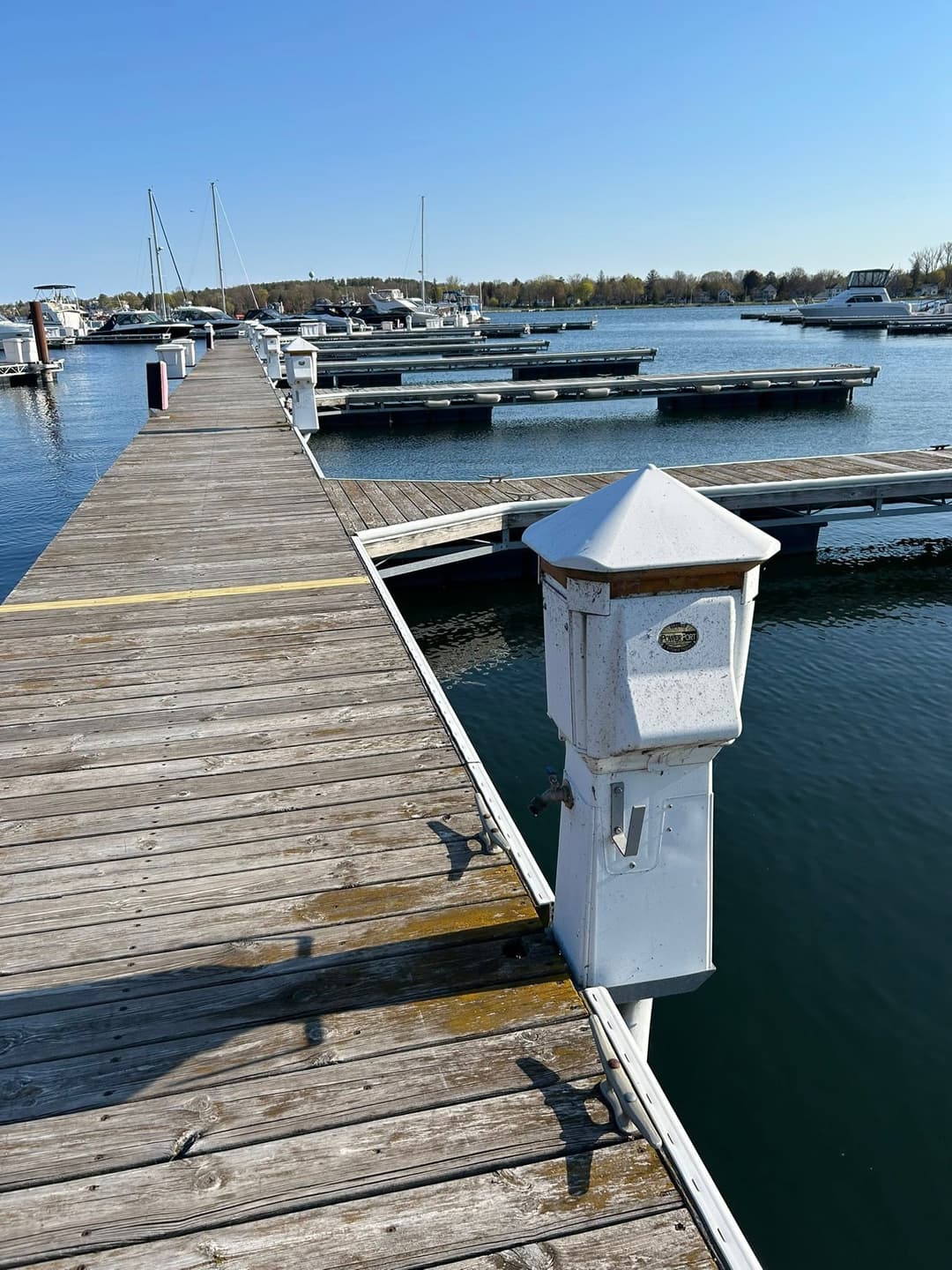 Wooden dock with white posts and boats in calm water on a sunny day.