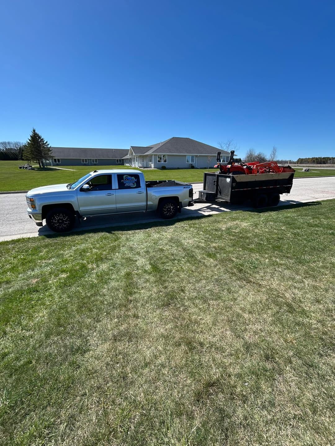 Silver pickup truck towing a trailer with lawn equipment in a residential area.